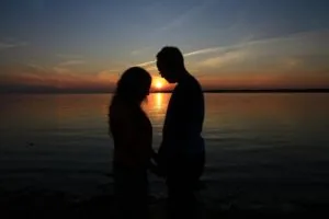 a picture of a couple praying in front of a body of water
