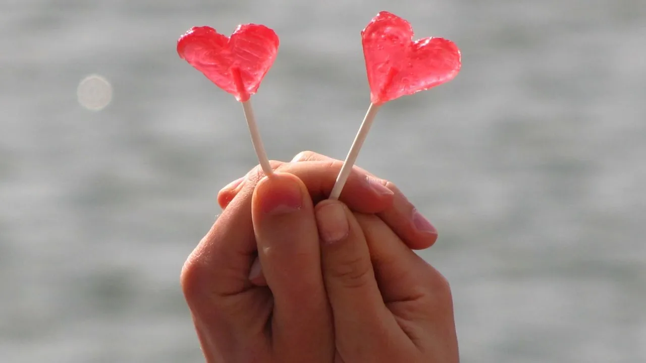 Two conjoined hands holding up heart shaped lollipop