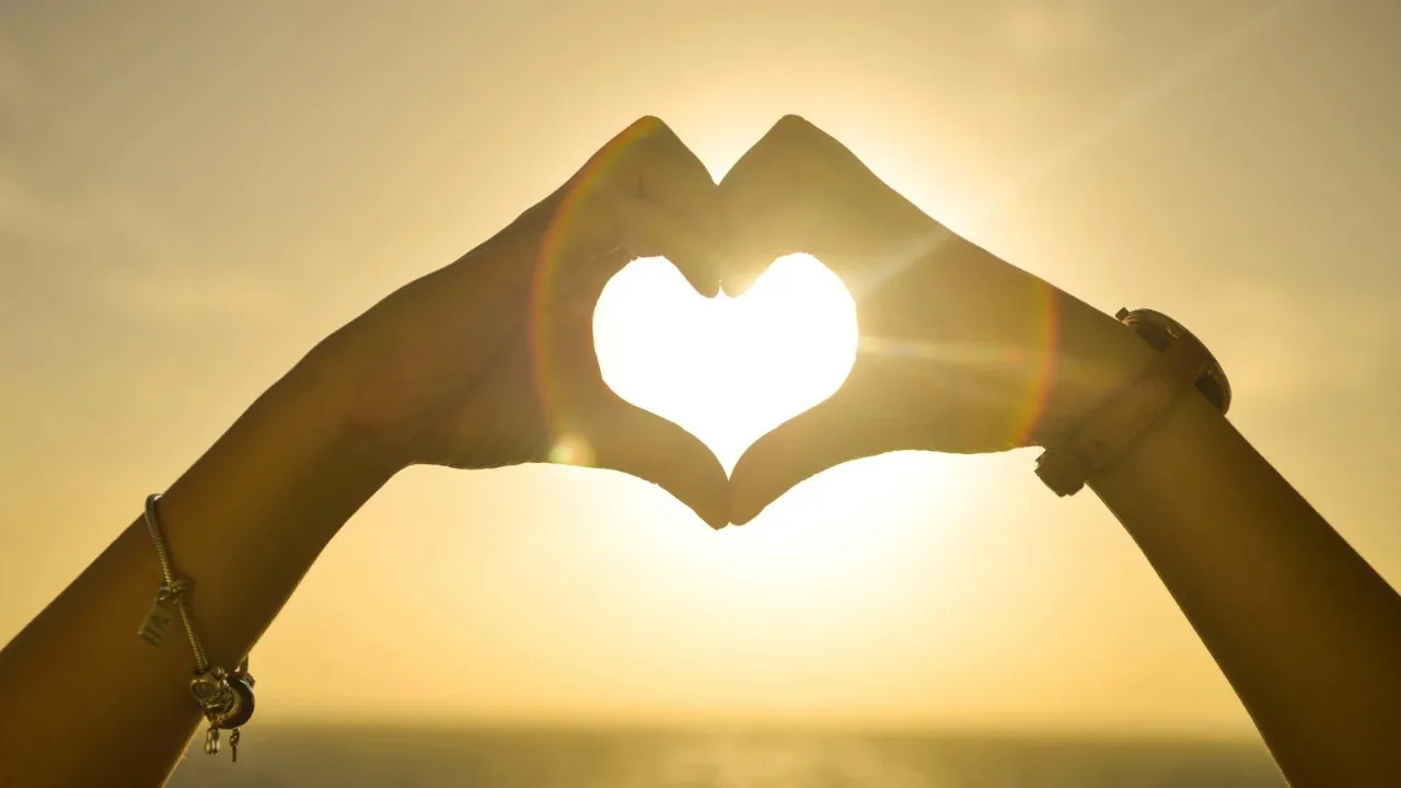 two hands form the heart shape against the sunset 