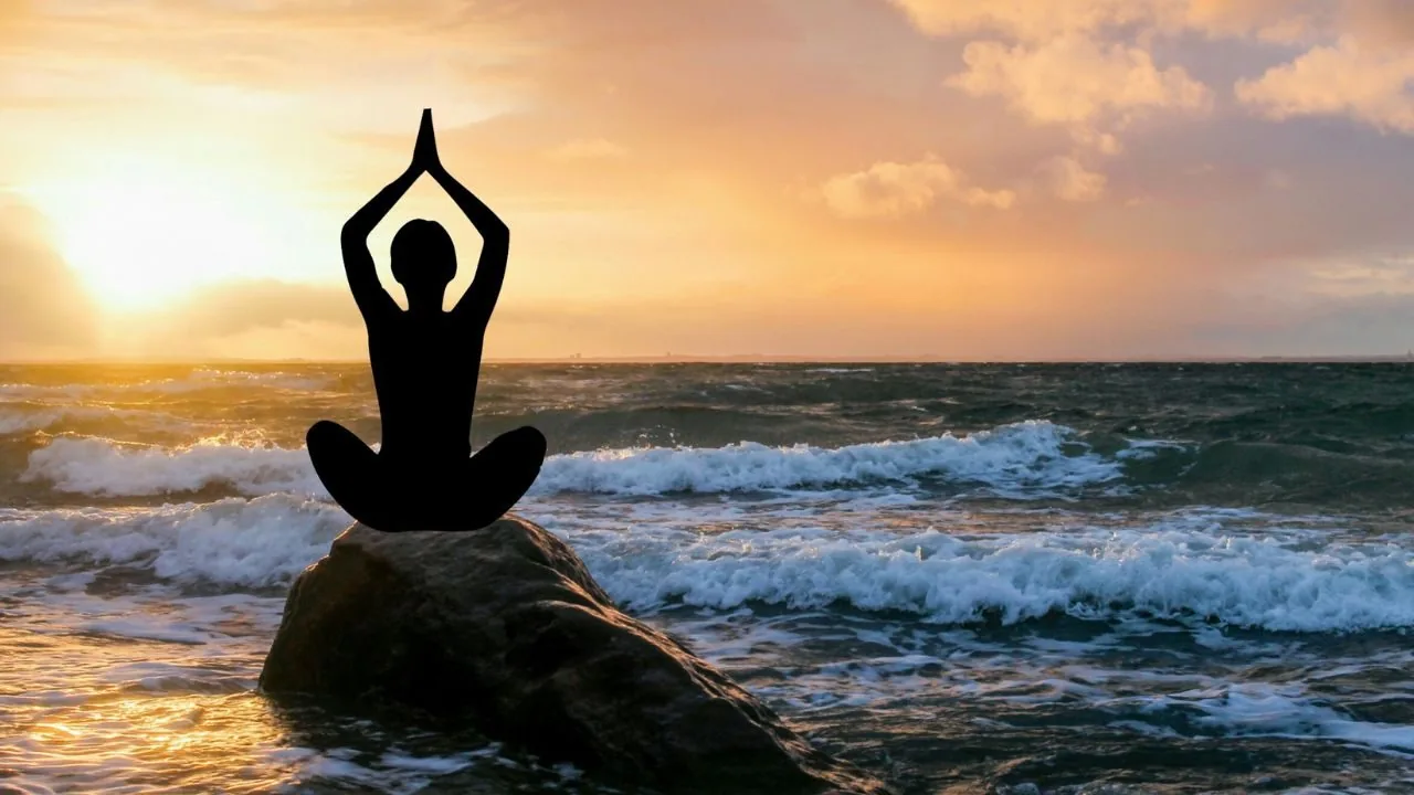 Silhouette of a woman doing yoga beside flowing water