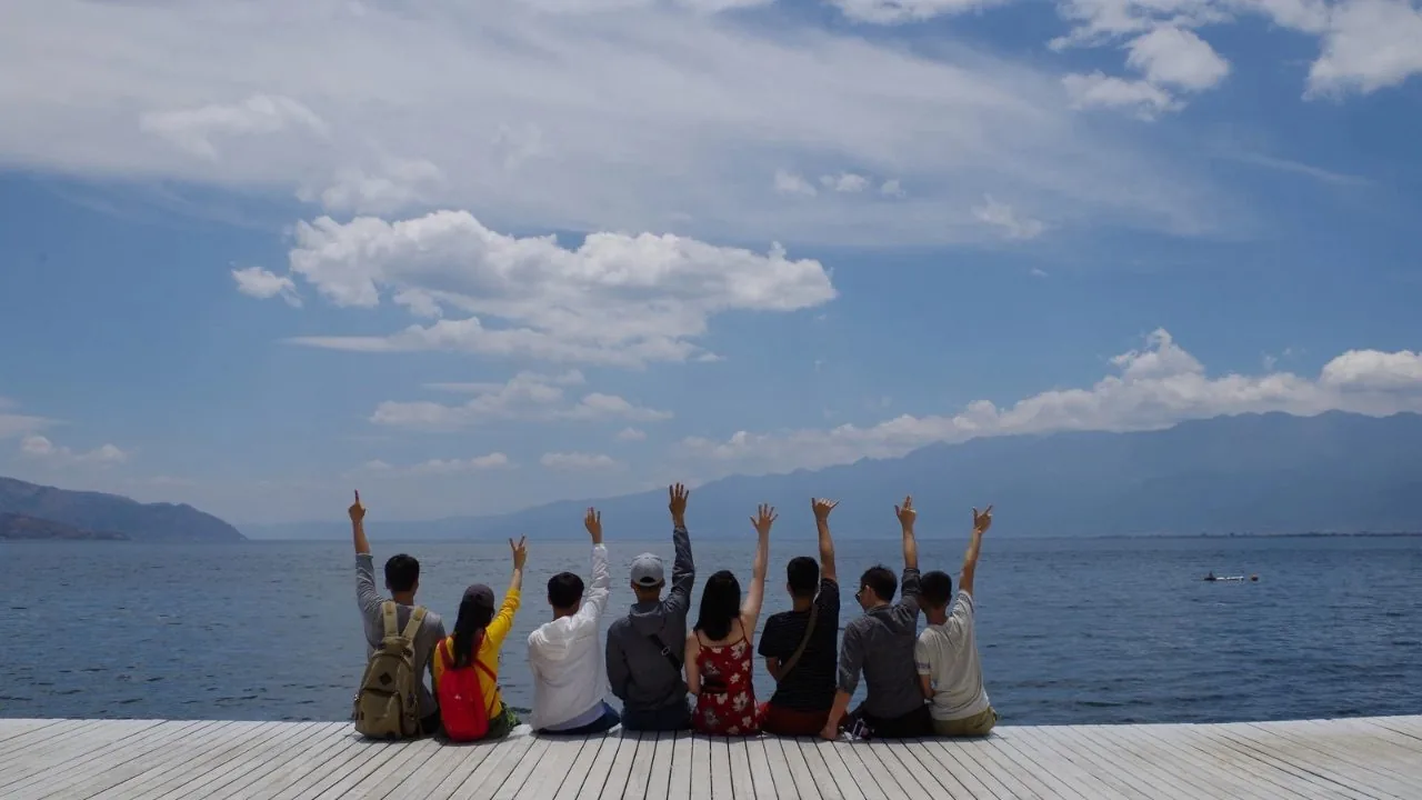 Friends sitting together facing the ocean, their backs against the camera 